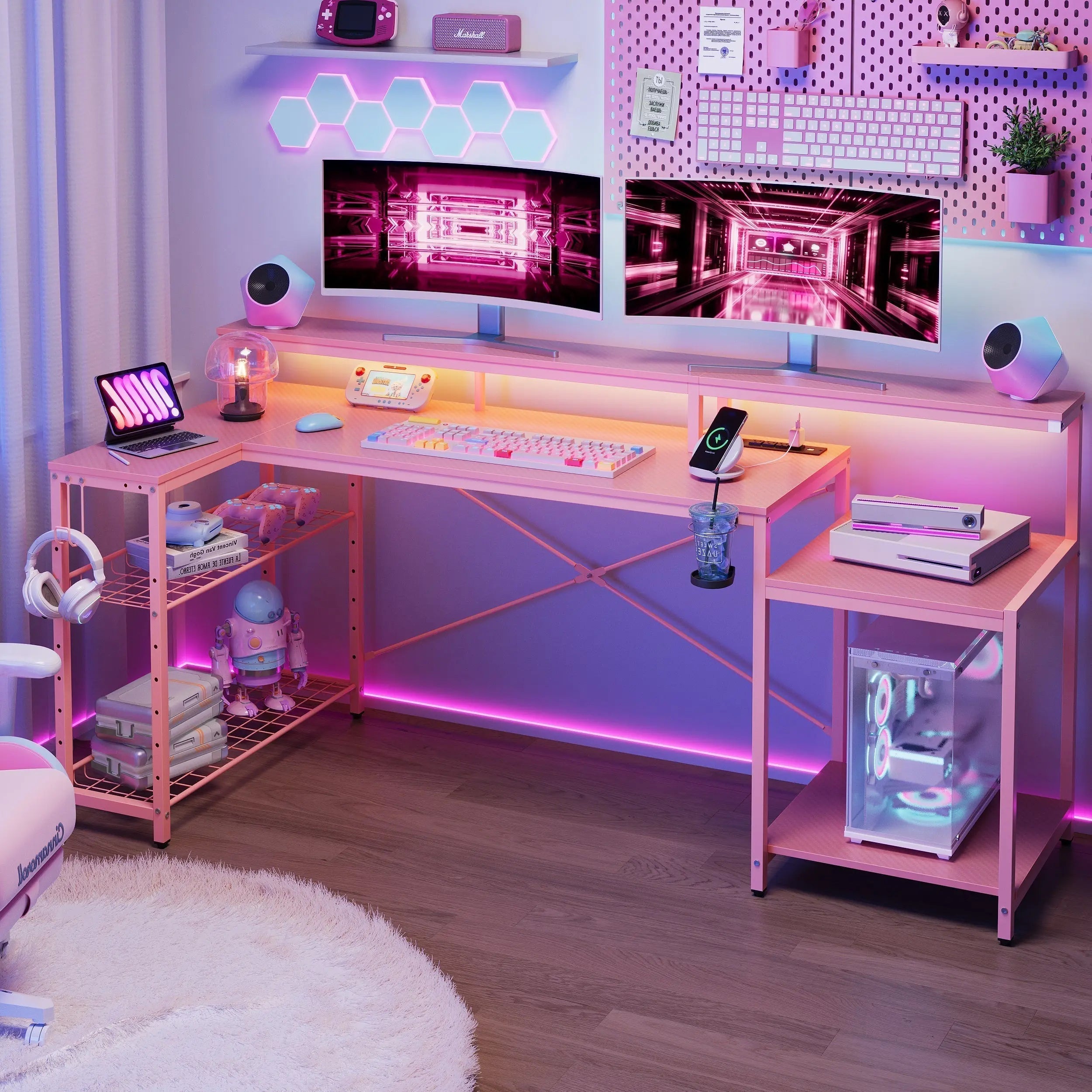 A complete pink L-shaped gaming desk setup with hutch, dual monitors, pink accessories, and vibrant RGB lighting in a gaming room.