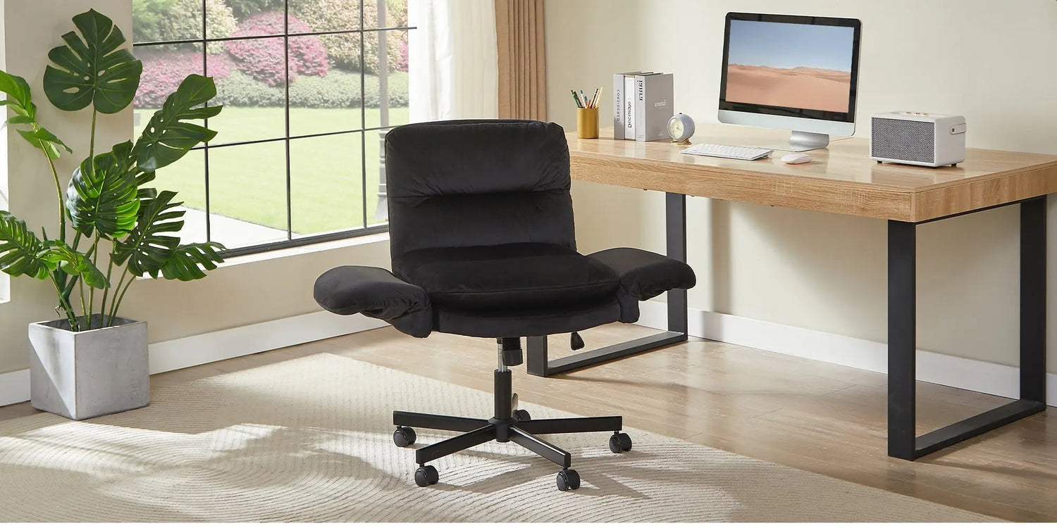 A wide black fabric ergonomic chair suitable for cross-legged sitting placed in a bright home office environment.